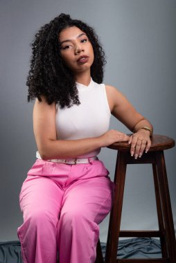 Güzel bir genç kadın, kıvırcık saçlı, stüdyoda gri bir arka planda poz veriyor..