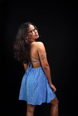 Düz saçlı, gözlüklü ve siyah arka planda mavi elbiseli güzel bir kadın..
