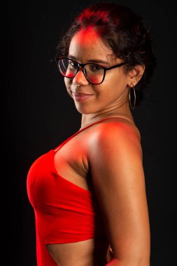 Güzel bir esmer kadın, reçeteli gözlük takıyor, kırmızı kıyafetler giyiyor, ayakta duruyor. Siyah arkaplanda izole.