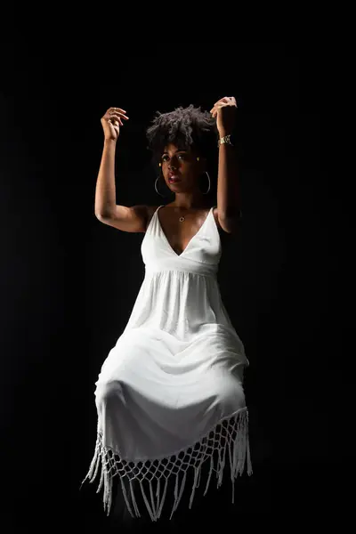 Beautiful woman, with black hair, sitting wearing white clothes and posing for the camera. isolated on black background.