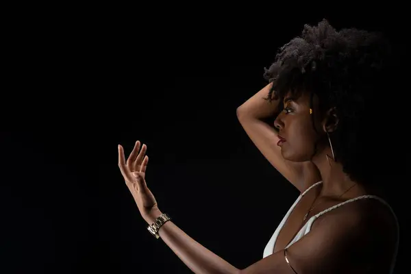 Beautiful woman, with black power hair, making movements with her arms. Wearing white clothes. Isolated on black background.