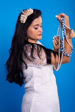 Kafasında deniz kabuğu tacı olan güzel, siyah saçlı kadın inci kolyelere bakıyor. Iemanja Özelleştirmesi.