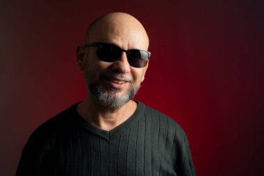 Beyaz, kel, güneş gözlüğü takan, kendine güvenen, kameraya bakan bir adam. Kırmızı arkaplanda izole.