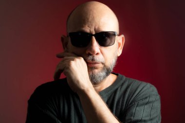 Beyaz, kel, güneş gözlüğü takan, kendinden emin ve ciddi bir şekilde kameraya bakıyor. Kırmızı arkaplanda izole.