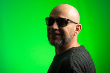 Beyaz, kel, güneş gözlüğü takan, kameraya gülümseyen bir adam. Yeşil arkaplanda izole.