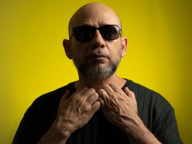 Beyaz, kel, güneş gözlüğü takan, kameraya gülümseyen bir adam. Sarı arkaplanda izole edilmiş.