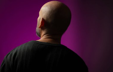 Yakışıklı, kel ve sakallı bir adam sırtı kameraya dönük yukarı bakıyor. Pembe arka planda izole edilmiş.