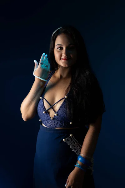 Portrait of beautiful woman with black hair and blue clothes, looking at the camera. Isolated on dark blue background.