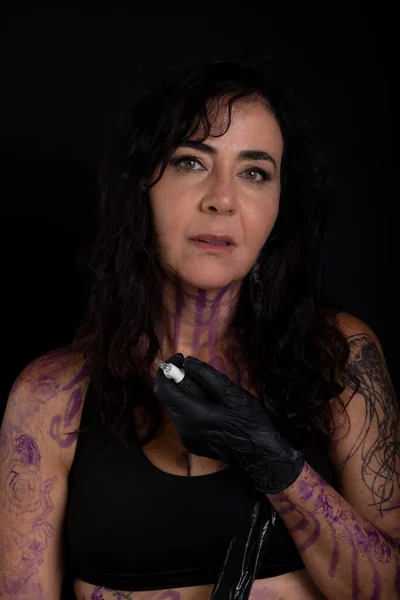 Beautiful artist holding tattoo machine looking at camera against black background