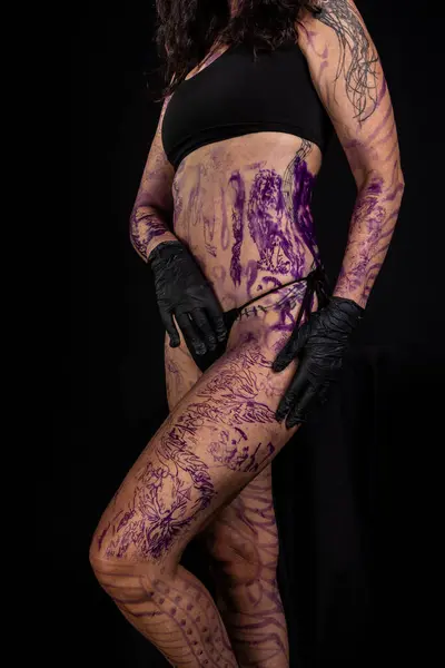 Part of woman\'s body painted and tattooed against black background