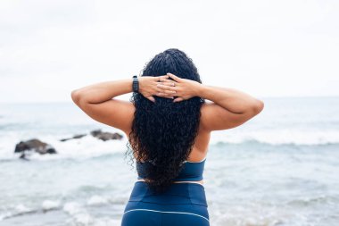 Güzel bir jimnastikçi kadın sahilde deniz ve bulutlu gökyüzüne karşı esneme hareketleri yapıyor. Sağlıklı yaşam tarzı.