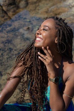 Güzel bir kadının portresi, örgülü ve mavi elbiseli, kumsalın kayalıklarında mavi gökyüzüne karşı poz veriyor..