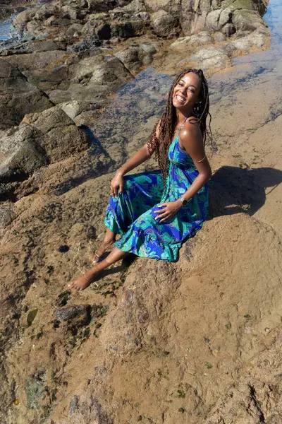 Güzel bir kadının portresi, örgülü ve mavi elbiseli, kumsalın kayalıklarında mavi gökyüzüne karşı poz veriyor..