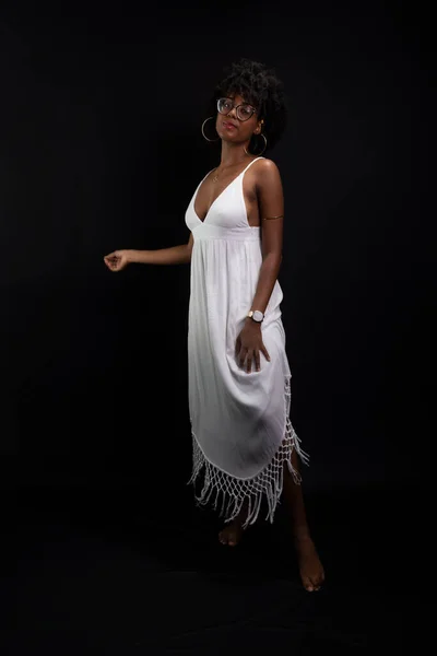 Beautiful beauty, with black power hair, standing moving her white dress against a black background.