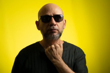 Beyaz, kel, güneş gözlüğü takan, kameraya gülümseyen bir adam. Sarı arkaplanda izole edilmiş.