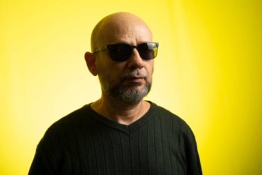 Beyaz, kel, güneş gözlüğü takan, kameraya gülümseyen bir adam. Sarı arkaplanda izole edilmiş.