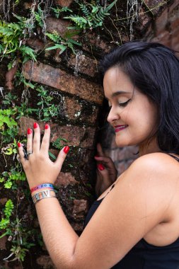 Güzel siyah saçlı kadın tuğladan yapılmış eski bir duvara dokunuyor. Keyifli bir yolculukta.