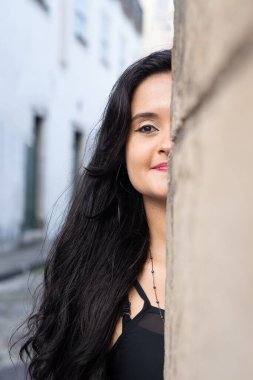 Güzel bir kadının yüzünün yarısının yakın plan portresi, siyah saçlı, dışarıda çimento duvara yaslanmış. Seyahat eden mutlu kişi.