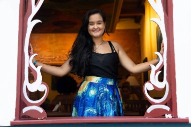 Süslü bir pencerenin kenarındaki güzel siyah saçlı kadın kameraya gülümsüyor. Seyahat eden kişi.