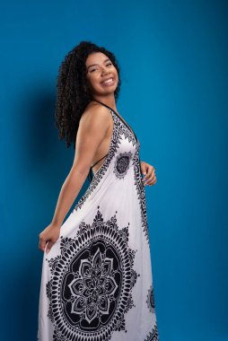 Fotoğraf için poz veren kıvırcık saçlı güzel bir genç kadının stüdyo portresi. Mavi arkaplanda izole.