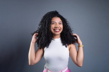 Kıvırcık saçlı, gülümseyen ve kameraya bakan güzel bir genç kadın. Gri arkaplanda izole.
