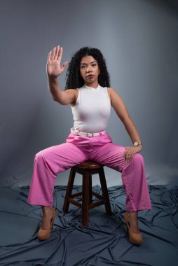 Güzel bir kadın oturuyor, sağ eliyle gri arka planda dur işareti yapıyor..