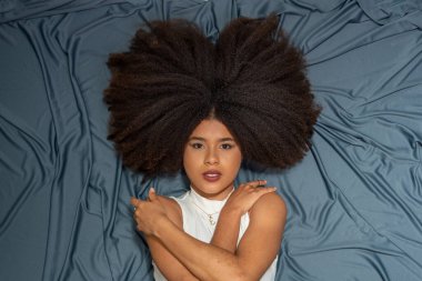 Güzel bir genç kadın, siyah saçlı, yerde yatan kameraya bakıyor gri bir bez arka planda..