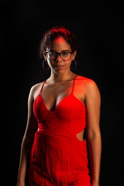 Güzel bir esmer kadın, reçeteli gözlük takıyor, kırmızı kıyafetler giyiyor, ayakta duruyor. Siyah arkaplanda izole.