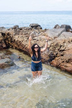 Kumsaldaki su birikintisinde güzel bir kadın, havaya su atıyor. Seyahat eden mutlu kişi.