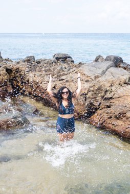 Kumsaldaki su birikintisinde güzel bir kadın, havaya su atıyor. Seyahat eden mutlu kişi.