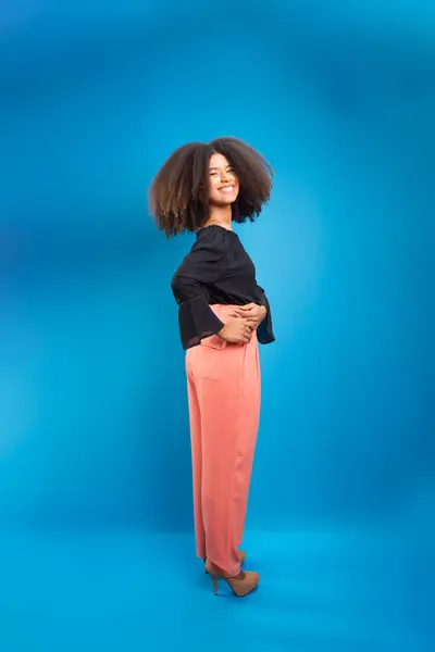 Beautiful young woman with black power hair, dressed formally. Isolated on blue background.