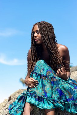 Mavi elbiseli ve örgülü saçlı güzel bir kadının portresi kumsalın kayalarında mavi gökyüzüne karşı oturuyordu..