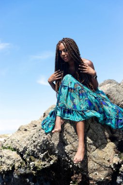 Mavi elbiseli ve örgülü saçlı güzel bir kadının portresi kumsalın kayalarında mavi gökyüzüne karşı oturuyordu..