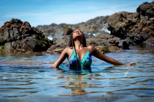Mavi elbiseli güzel bir kadın ve kumsal suyunda yarı vücut olan örgülü saçlar. Seyahat eden kişi.