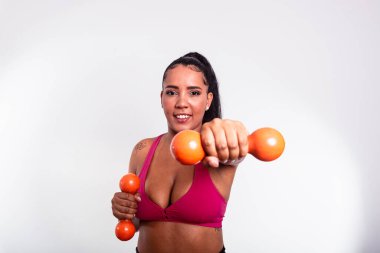 Güzel bir kadın, spor kıyafetleri içinde, dambılları kameraya doğru tutuyor. Fiziksel egzersizle sağlıklı bir hayat..