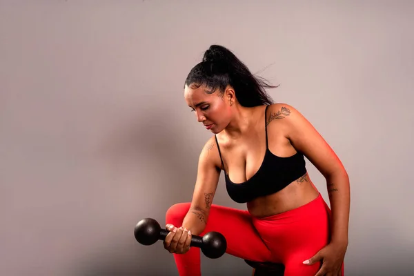 Beautiful brunette woman, in gym clothes, sitting doing exercises with dumbbells. Healthy life. Against gray background.