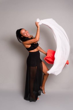 Siyah elbiseli esmer kadın gri arka planda beyaz ve turuncu elbiseli jimnastik hareketler yapıyor..