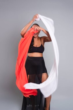 Siyah elbiseli esmer kadın gri arka planda beyaz ve turuncu elbiseli jimnastik hareketler yapıyor..