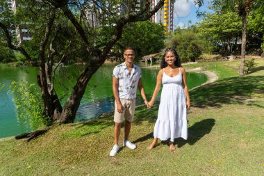 Dışarıda fotoğraf çektirmek için el ele tutuşan bir çift. Bir bebek bekliyorlar. Vahiy Çayı.