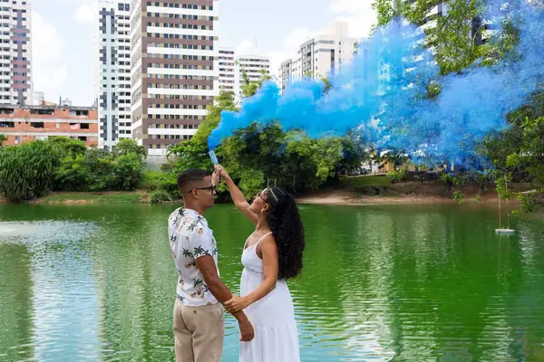 Happy couple having a gender reveal party. blue smoke grenade outdoors. It\'s a boy. Gender reveal party concept. Couple in love