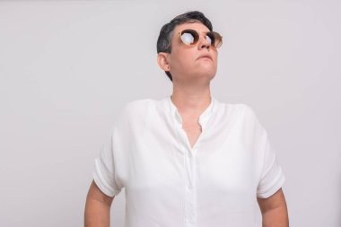 Işıklı arka planda açık renk kıyafetler ve güneş gözlüğü takan güzel kadın..