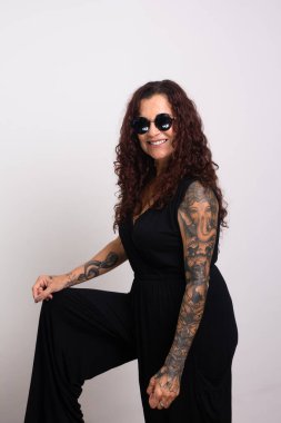 Güzel kıvırcık saçlı, güneş gözlüğü takan ve gülümseyen siyah elbiseli bir kadın. Beyaz arkaplanda izole.