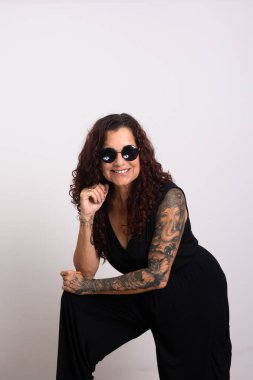 Güzel kıvırcık saçlı, güneş gözlüğü takan ve gülümseyen siyah elbiseli bir kadın. Beyaz arkaplanda izole.