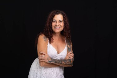 Güzel, olgun, kıvırcık kızıl saçlı ve kollarını kavuşturmuş kameraya bakan bir kadın. Siyah arkaplanda izole.