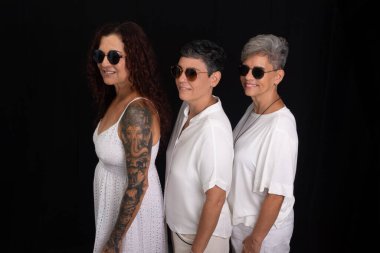 Siyah arka planda güneş gözlüğü takan beyaz elbiseli üç güzel kadın..