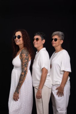 Siyah arka planda güneş gözlüğü takan beyaz elbiseli üç güzel kadın..
