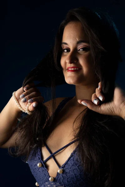 Portrait of beautiful woman with black hair and blue clothes, looking at the camera. Isolated on dark blue background.