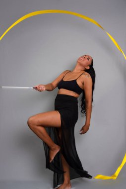 Güzel bir jimnastikçi kadın sarı kurdeleyle daireler çiziyor. Gri arkaplanda izole.