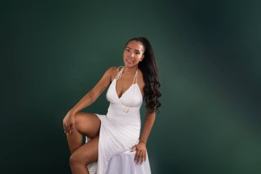 Güzel esmer kadın, elleri dizlerinin üstünde oturmuş fotoğraf için poz veriyor. Yeşil arkaplanda izole.