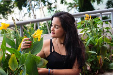 Güzel siyah saçlı kadın, yeşil bitkilerin arasında, sarı bir çiçek kokluyor. Keyifli bir yolculukta.